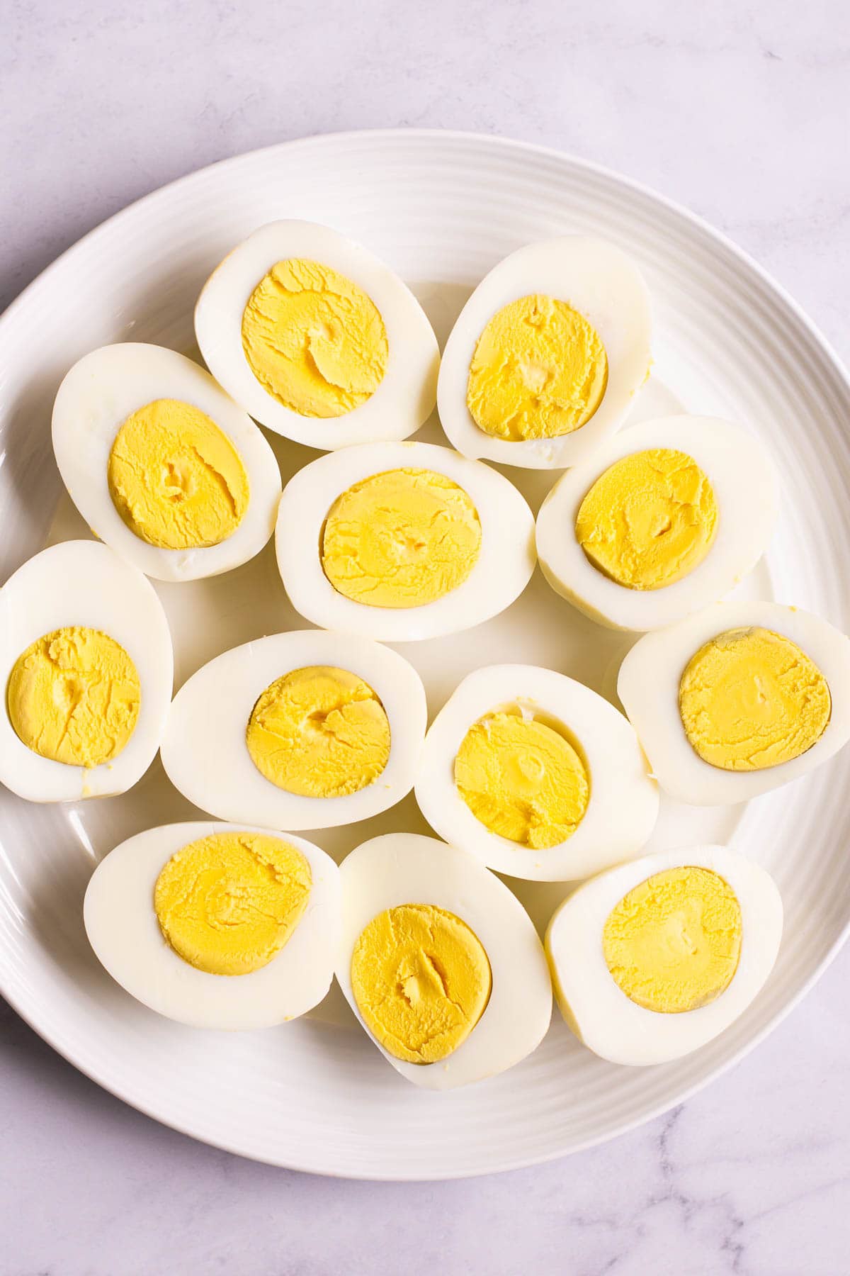 Instant pot hard boiled eggs cut in halves on white plate.