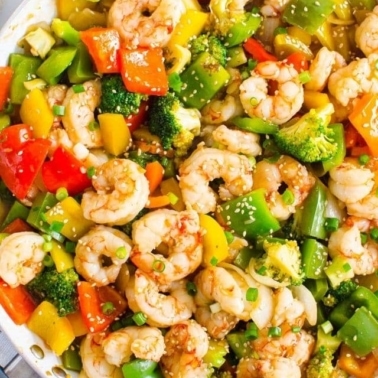 Shrimp and vegetables of broccoli and bell peppers in skillet garnished with sesame seeds.