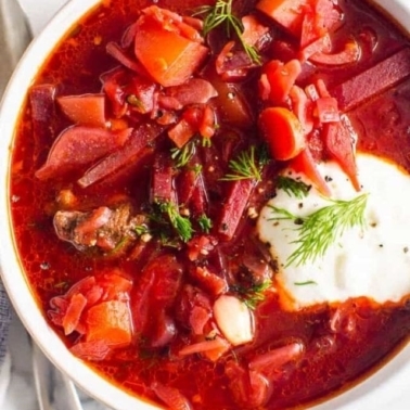 Borscht in a white soup bowl with sour cream and a sprig of dill.