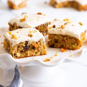 Three healthy carrot cake bars on white cake stand.