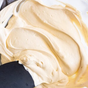 Healthy cream cheese frosting stirred by black spatula in glass bowl.