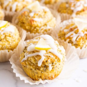 Healthy lemon poppy seed muffins unwrapped with icing and fresh lemon.