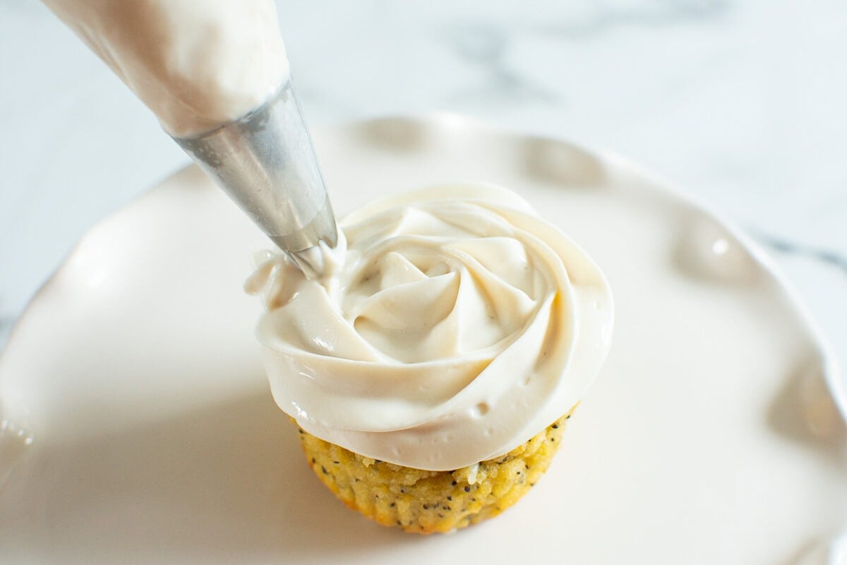 Piping Greek yogurt frosting on lemon poppy seed muffin with piping bag.