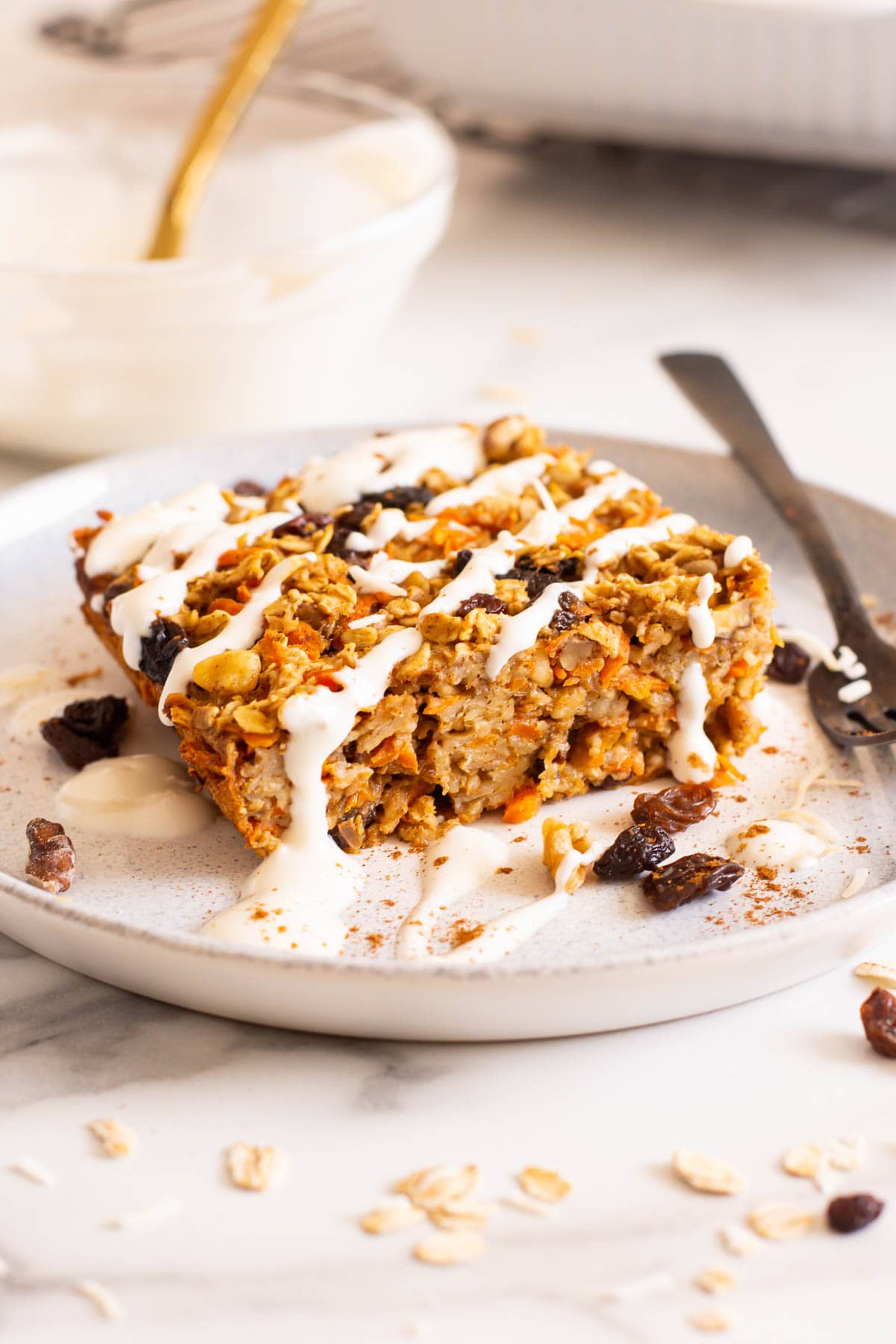 A slice of carrot cake baked oatmeal with a drizzle on white plate. 