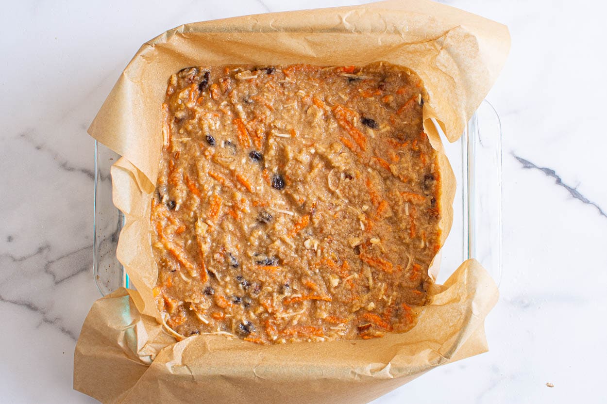 Unbaked carrot cake bar batter in parchment paper lined square baking dish.