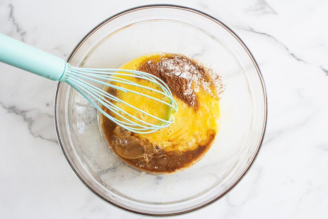 Eggs, maple syrup, oil, vanilla, cinnamon and baking staples whisked in bowl.