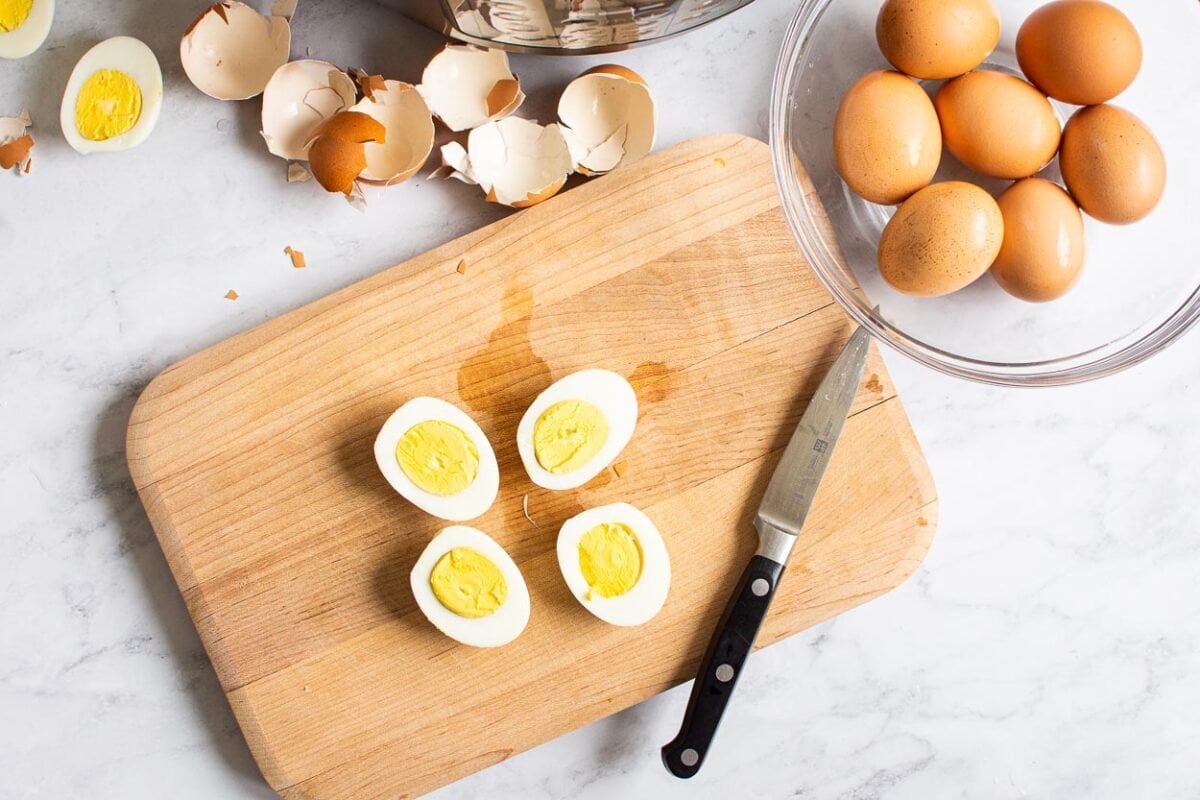 Hard boiled eggs cut in halves on a cutting board, eggs in a bowl and egg shells on a counter.