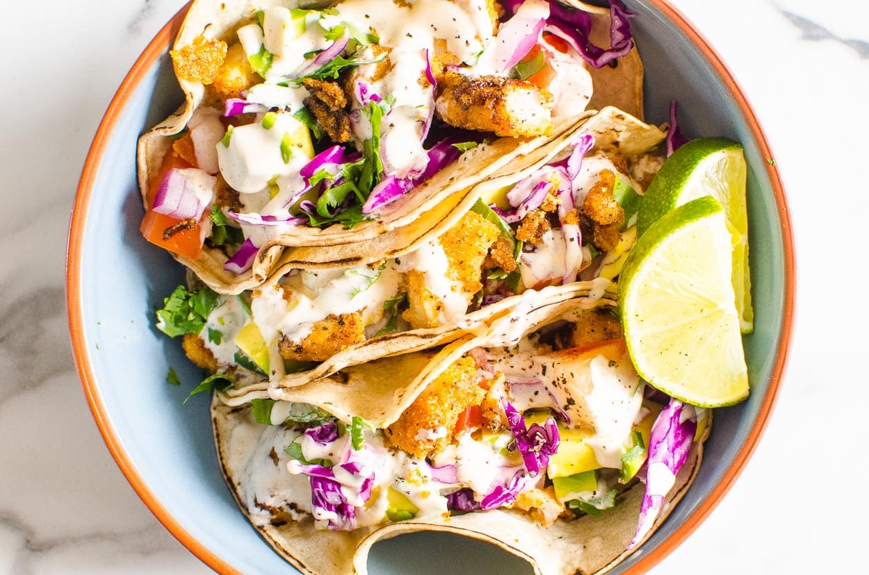 Fish taco recipe served with crema, fixings and lime in a blue bowl.
