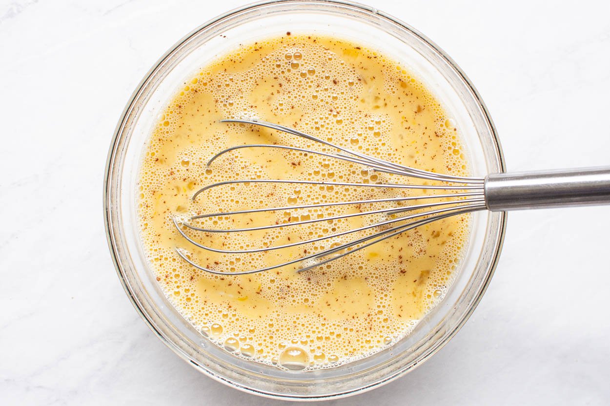 Eggs, maple syrup, almond milk, cinnamon and vanilla being whisked in bowl.