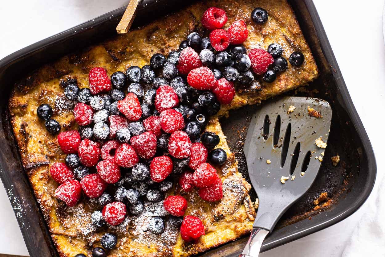 A dish of healthy french toast casserole topped with berries and a serving spatula.