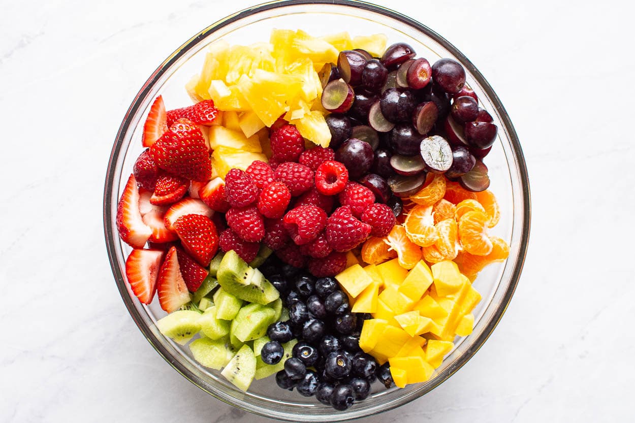 Cut grapes, pineapple, mango, mandarins, kiwi and berries in bowl.