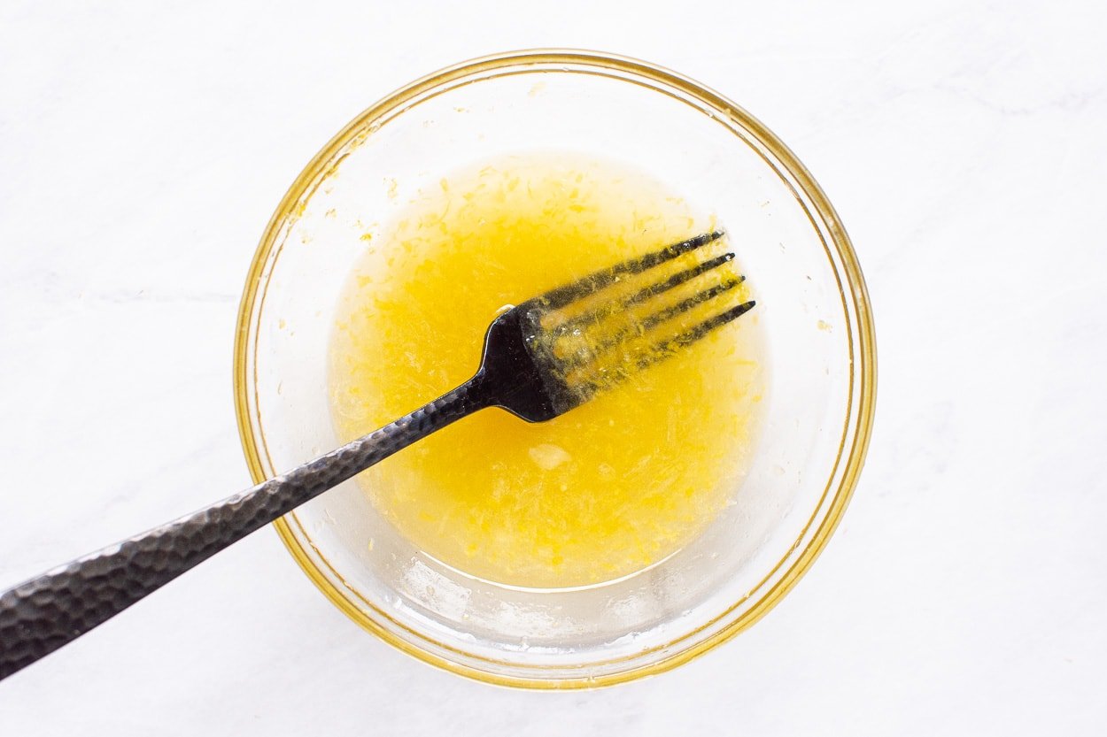 Lemon juice, lemon zest and honey with fork in bowl.