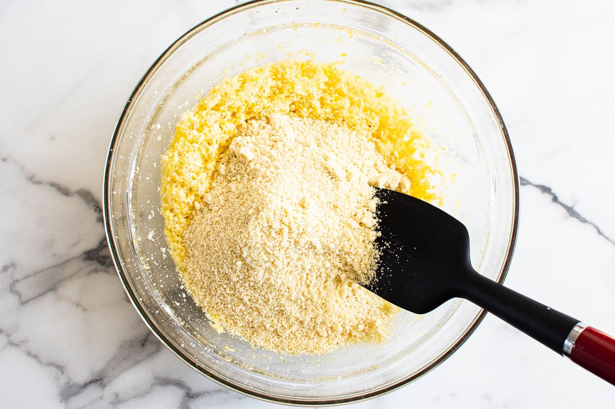 Beaten butter with sugar and egg, almond flour in glass bowl and black spatula.