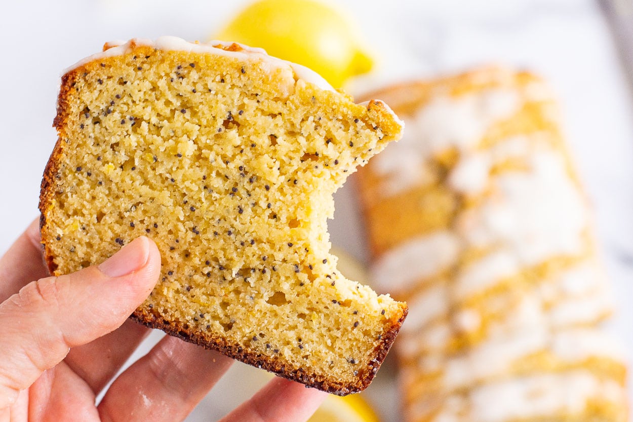 A hand holding a slice of healthy lemon poppy seed bread with a bite missing. 