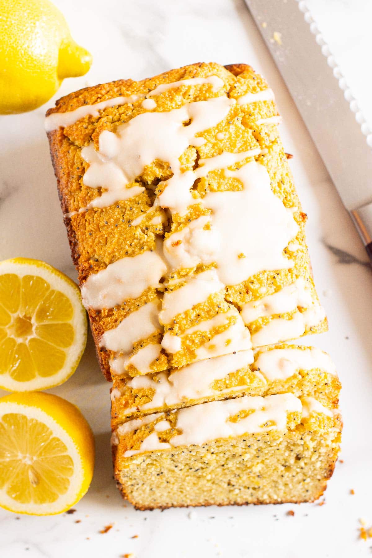 Sliced healthy lemon poppy seed bread with glaze, fresh lemons and knife.