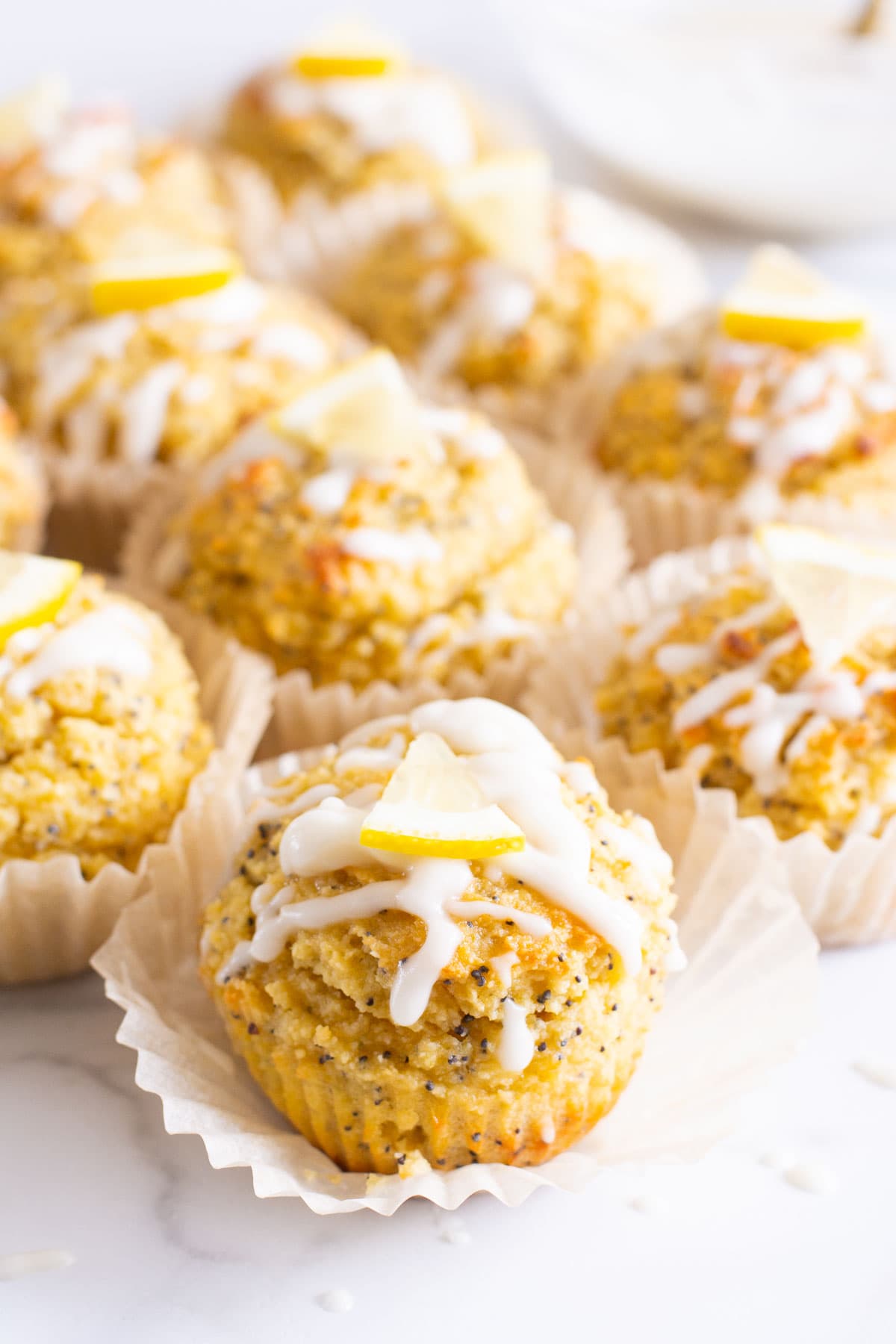 Healthy lemon poppy seed muffins with glaze and fresh lemon garnish on top. 