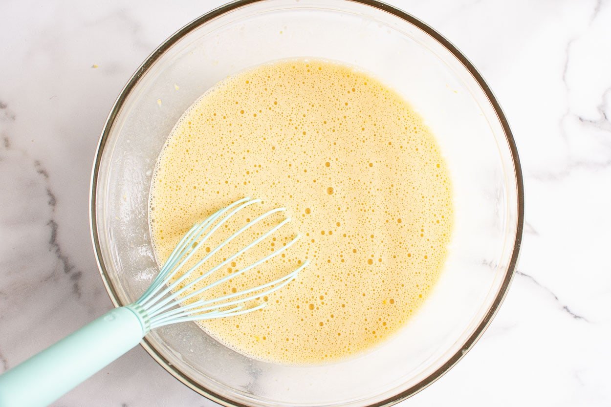 Whisked liquids for lemon poppy seed muffins batter in glass bowl and a whisk.