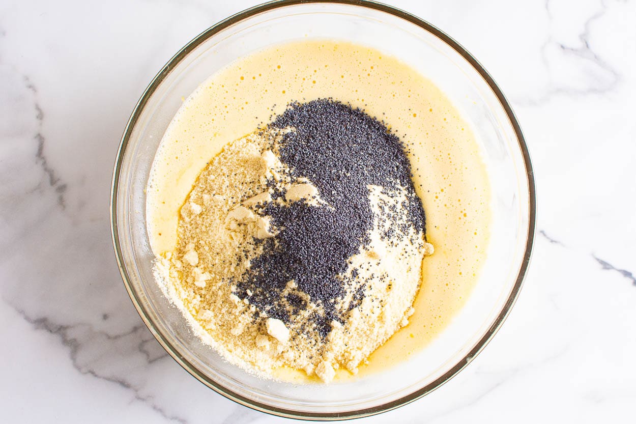 Liquid batter ingredients, poppy seeds and almond flour in glass bowl.