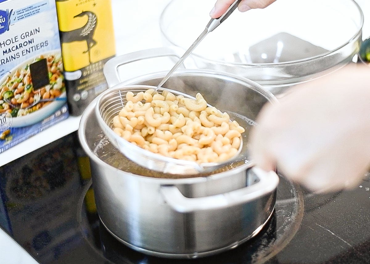 Checking for doneness cooked elbow macaroni in a colander over a pot of water.