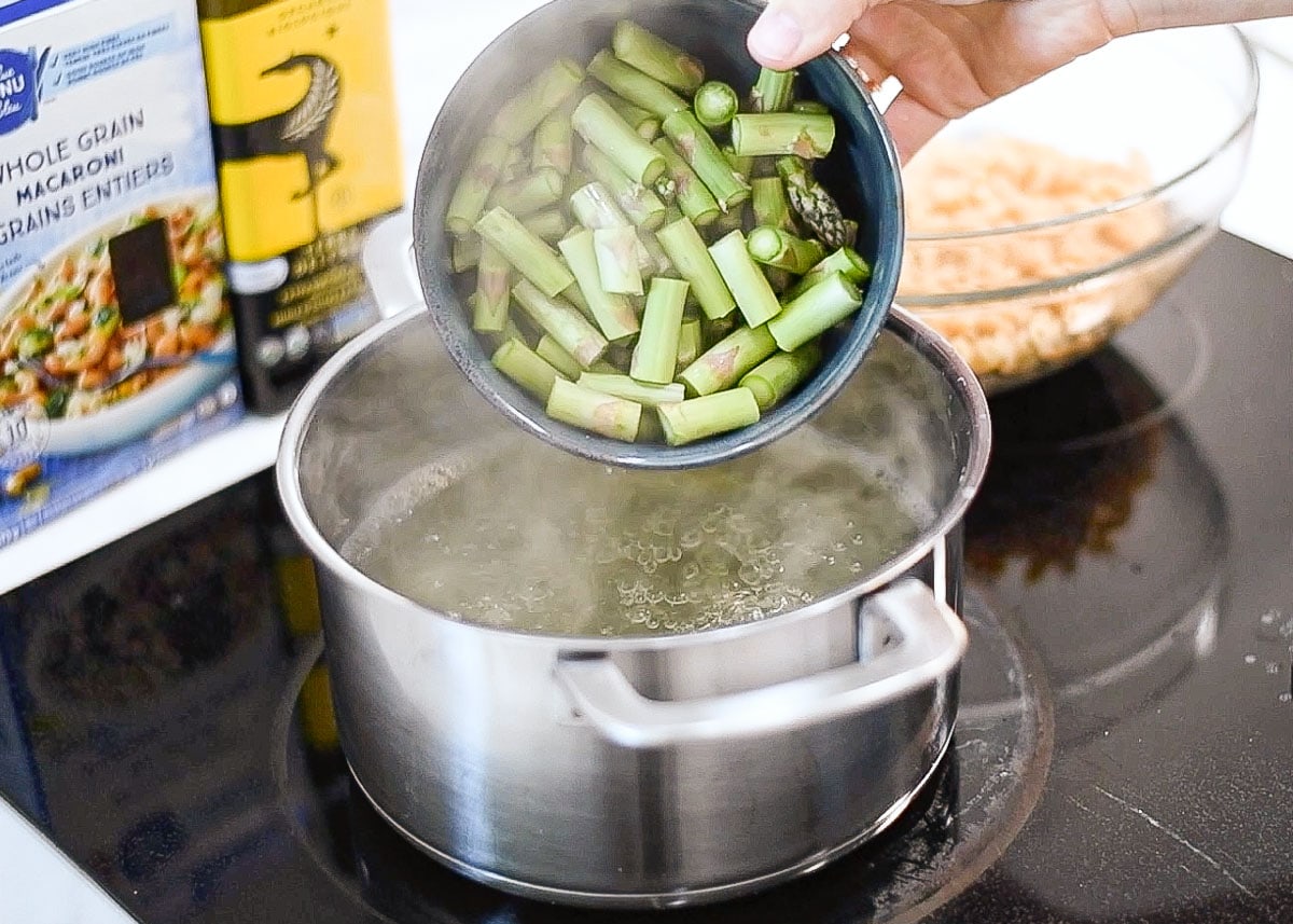 Adding chopped asparagus into a pot with boiling pasta water.
