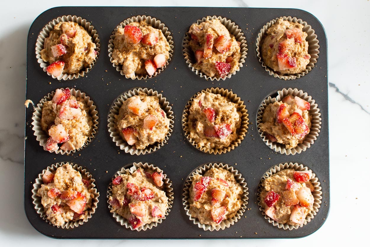 Muffin batter with strawberries in a muffin tin.