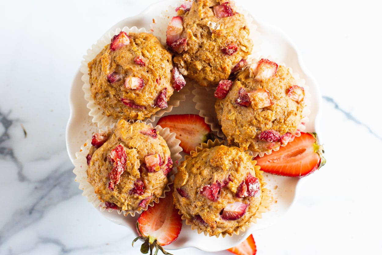 Looking down at 5 healthy strawberry muffins on a white serving stand.