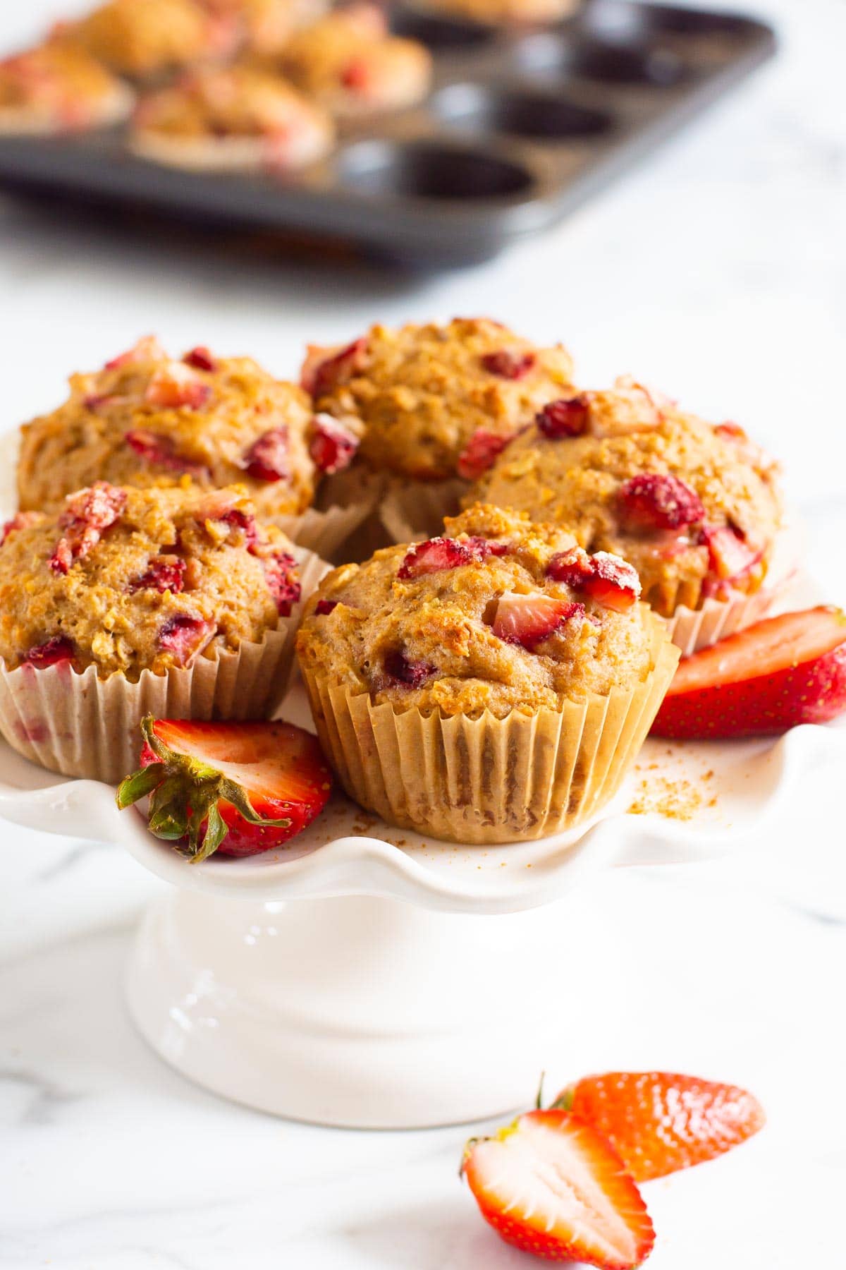 Healthy strawberry muffins on a white stand with muffin tin in background.