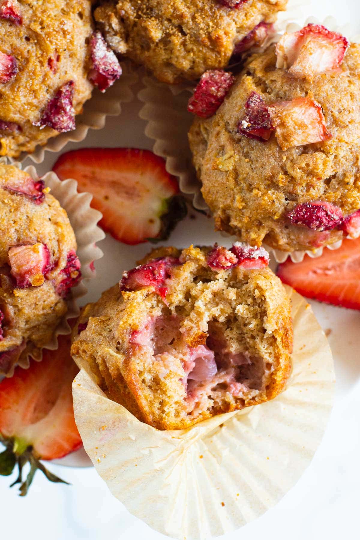 Healthy strawberry muffins with one unwrapped from liner and a bite missing.