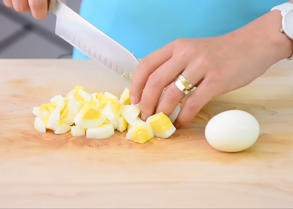 Chopping hard boiled eggs on a cutting board.
