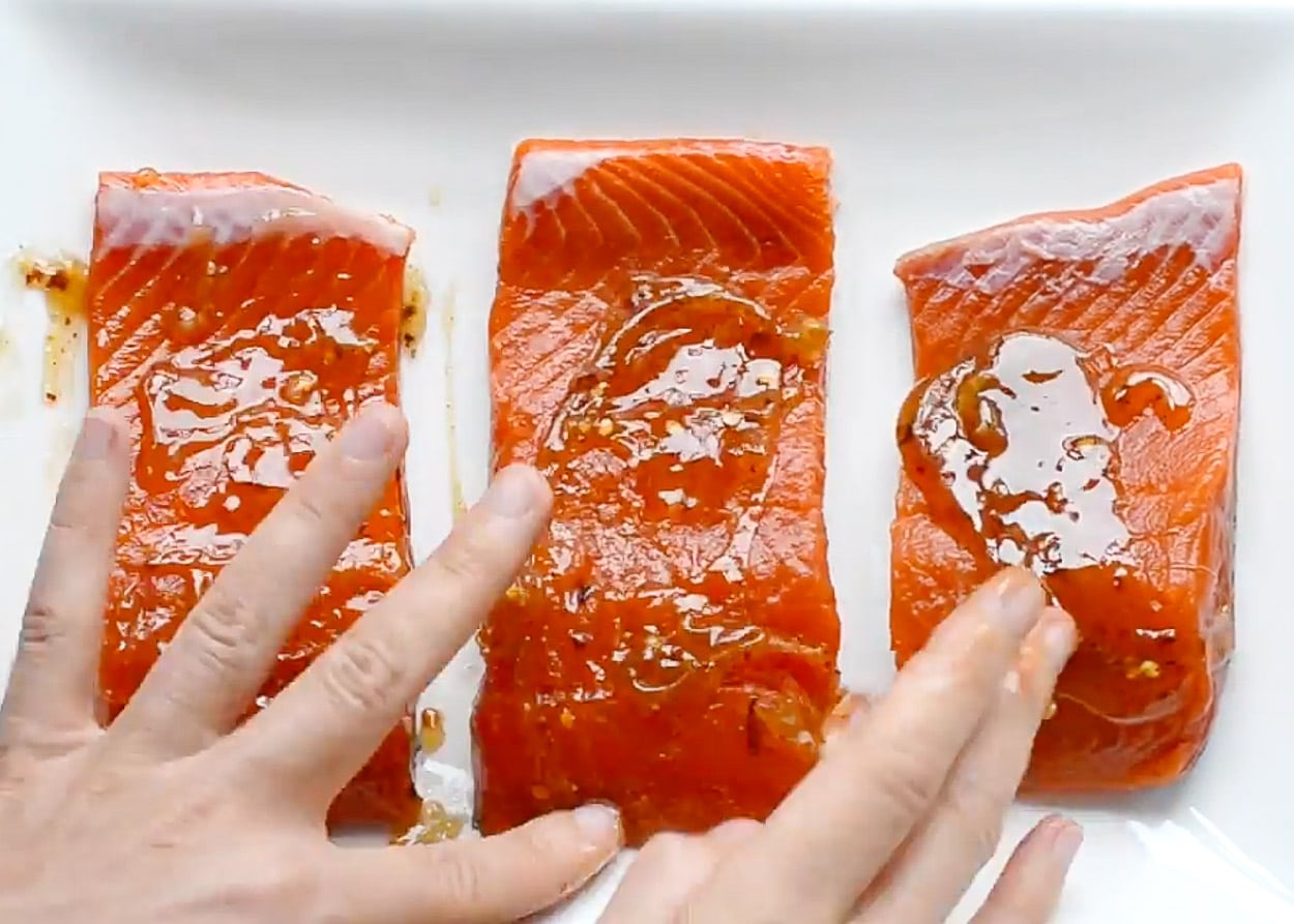 Spreading thai sweet chili sauce on each salmon fillet with hands.