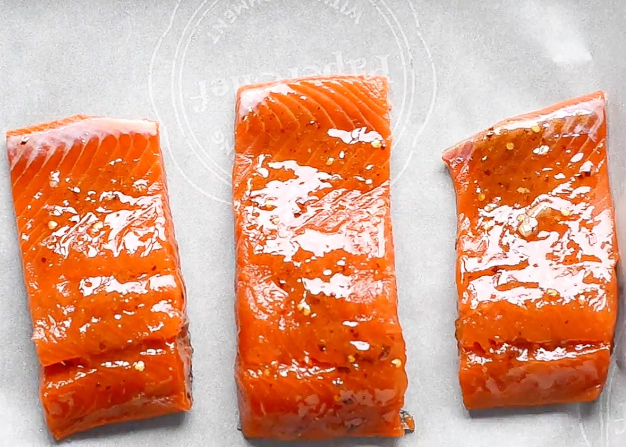 Coated in Thai sauce salmon fillets on parchment lined baking tray.