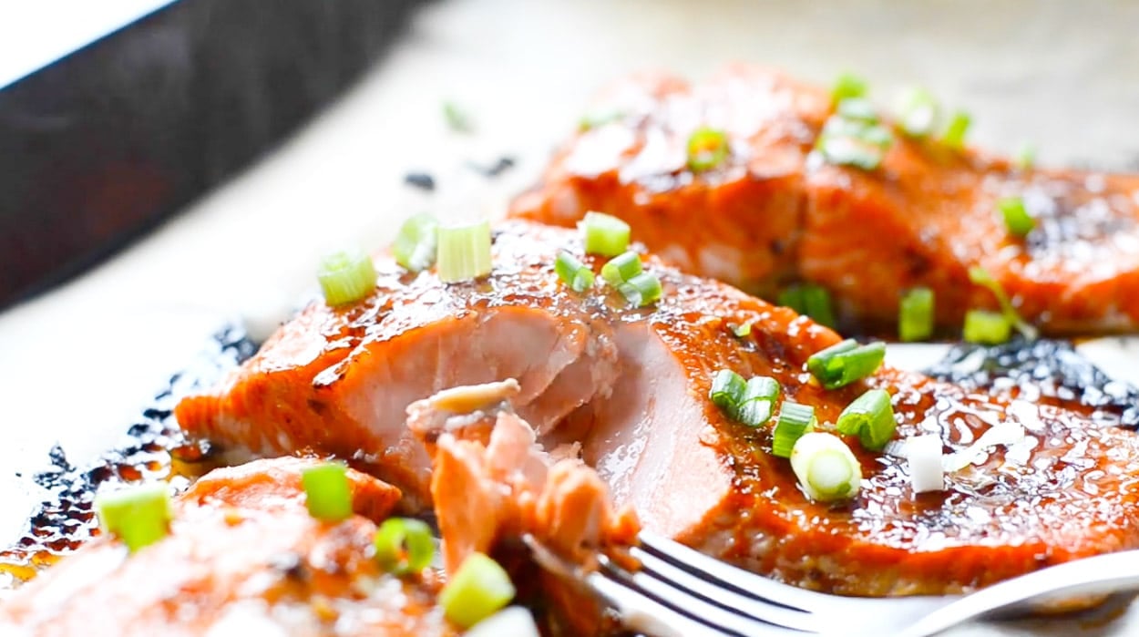 A slice of sweet chili salmon garnished with green onion and fork taking a piece out of it.