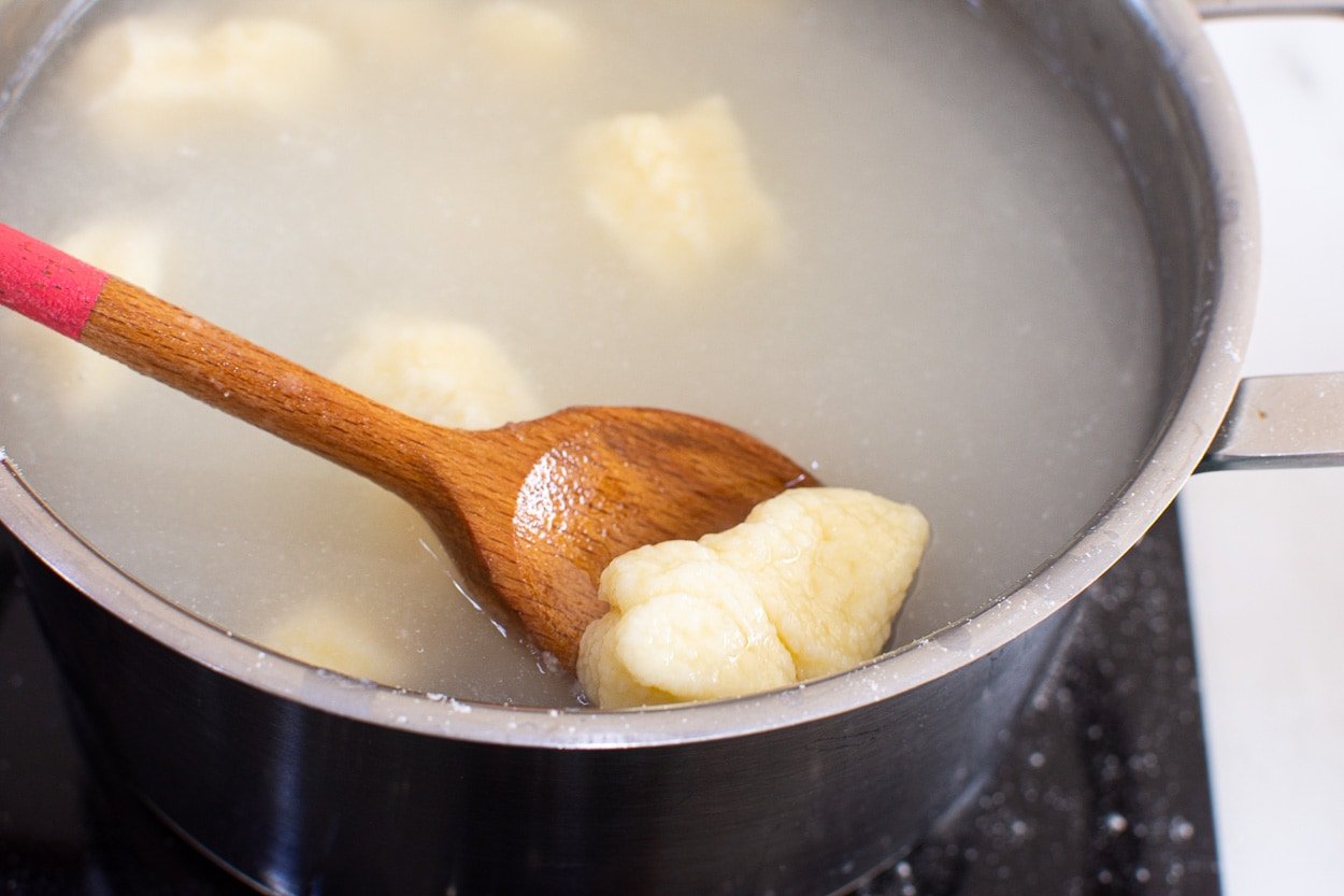 Lazy pierogi on a wooden spoon inside the pot with water.