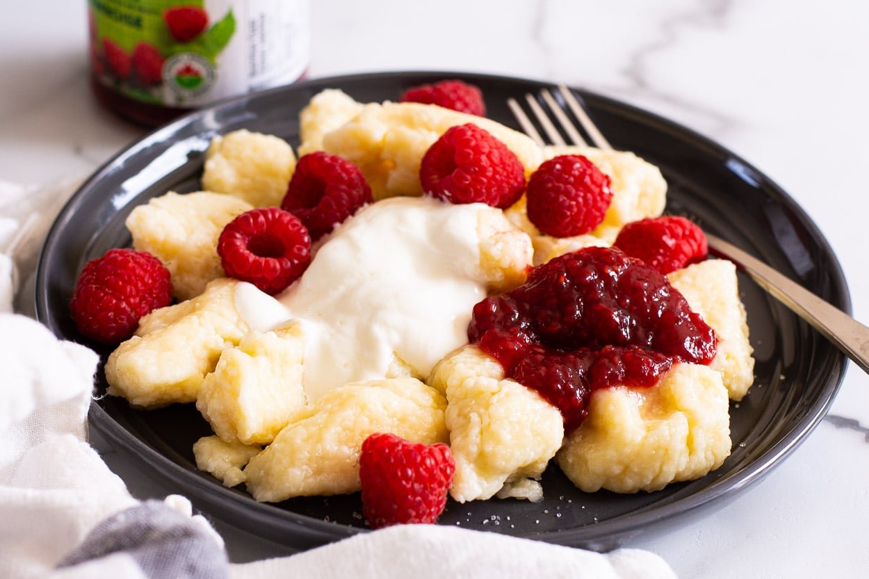 Lazy pierogi with yogurt, raspberries and jam on a plate with a fork.