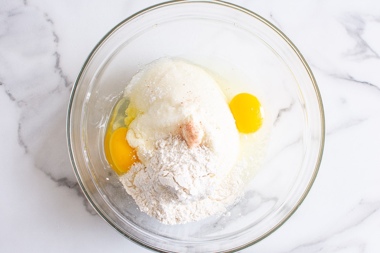 Ricotta cheese, eggs, flour, sugar and salt in glass bowl.