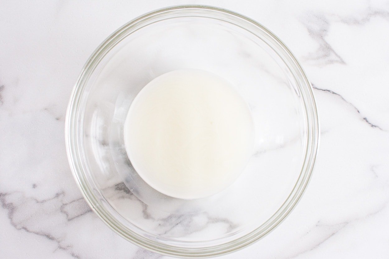 A glass bowl with drained whey on a counter.