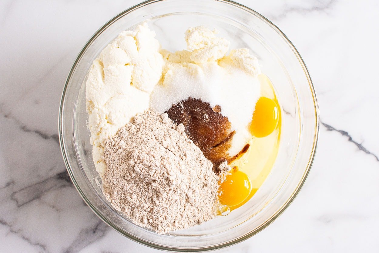 Drained ricotta cheese, eggs, flour, sugar and vanilla extract in glass bowl.