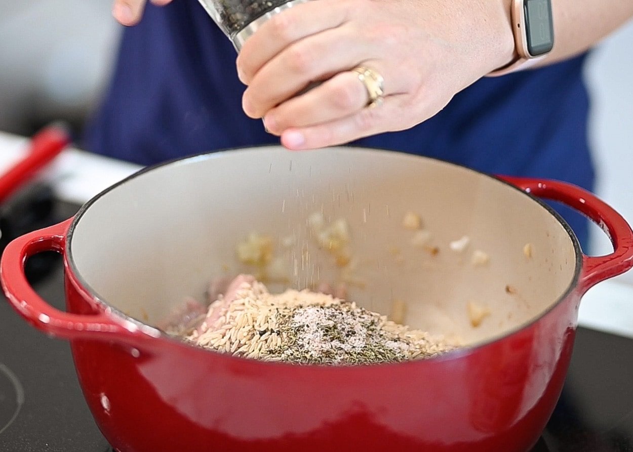 Adding seasoning on top of meat, rice, veggies in red pot.