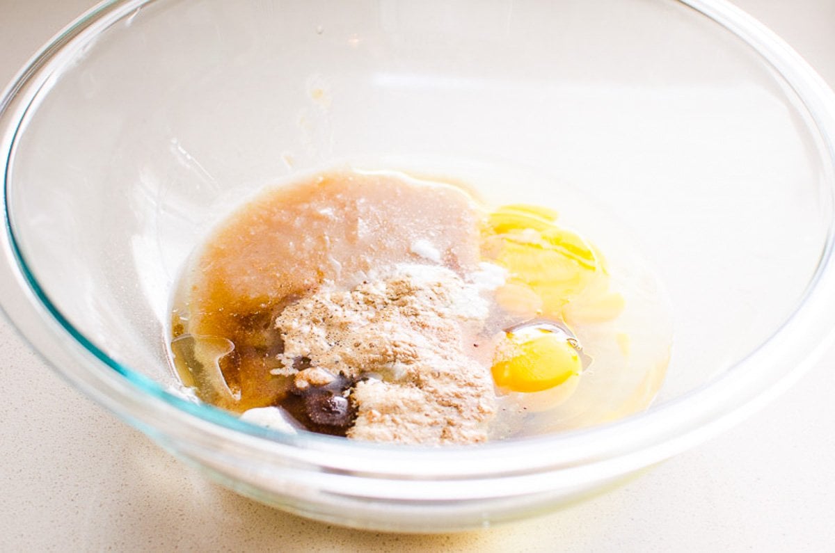 A mixing bowl with eggs, applesauce, maple syrup, oil, extract, baking powder, soda, cinnamon and salt.