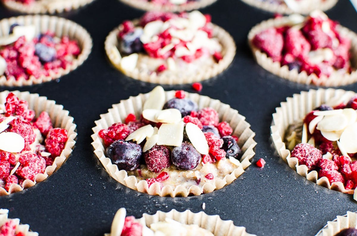 Unbaked muffins with berries and sliced almonds in a muffin tin.