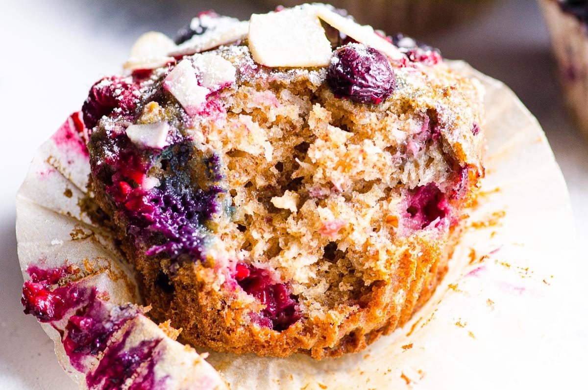 Almond muffin with berries unwrapped in a liner and a bite taken out of.