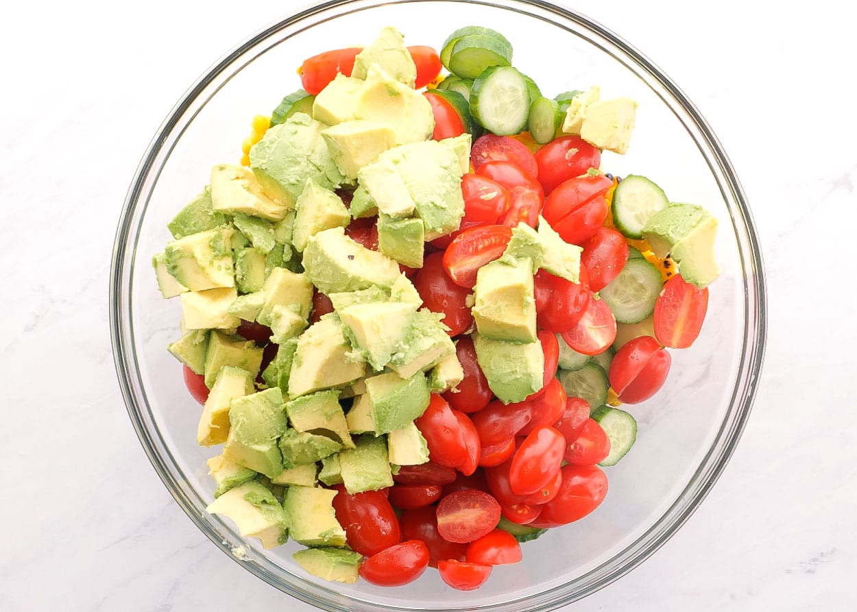 Diced avocado, tomato, cucumber and corn in glass bowl.