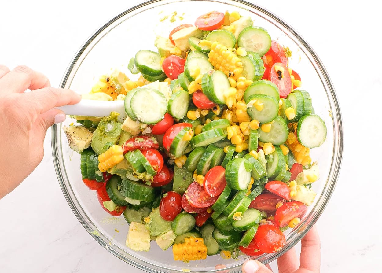Stirring avocado corn salad ingredients with a spoon in a bowl.