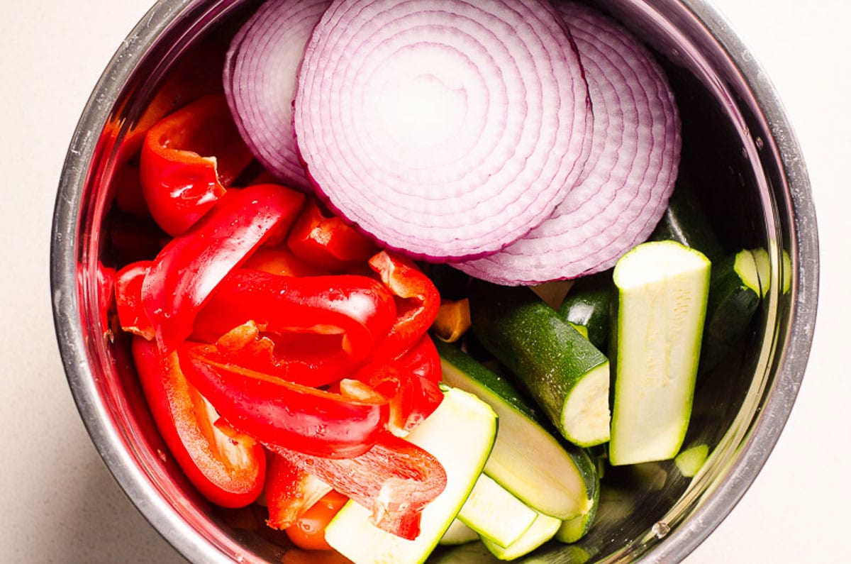 Sliced zucchini, red onion, and red bell peppers in a bowl.