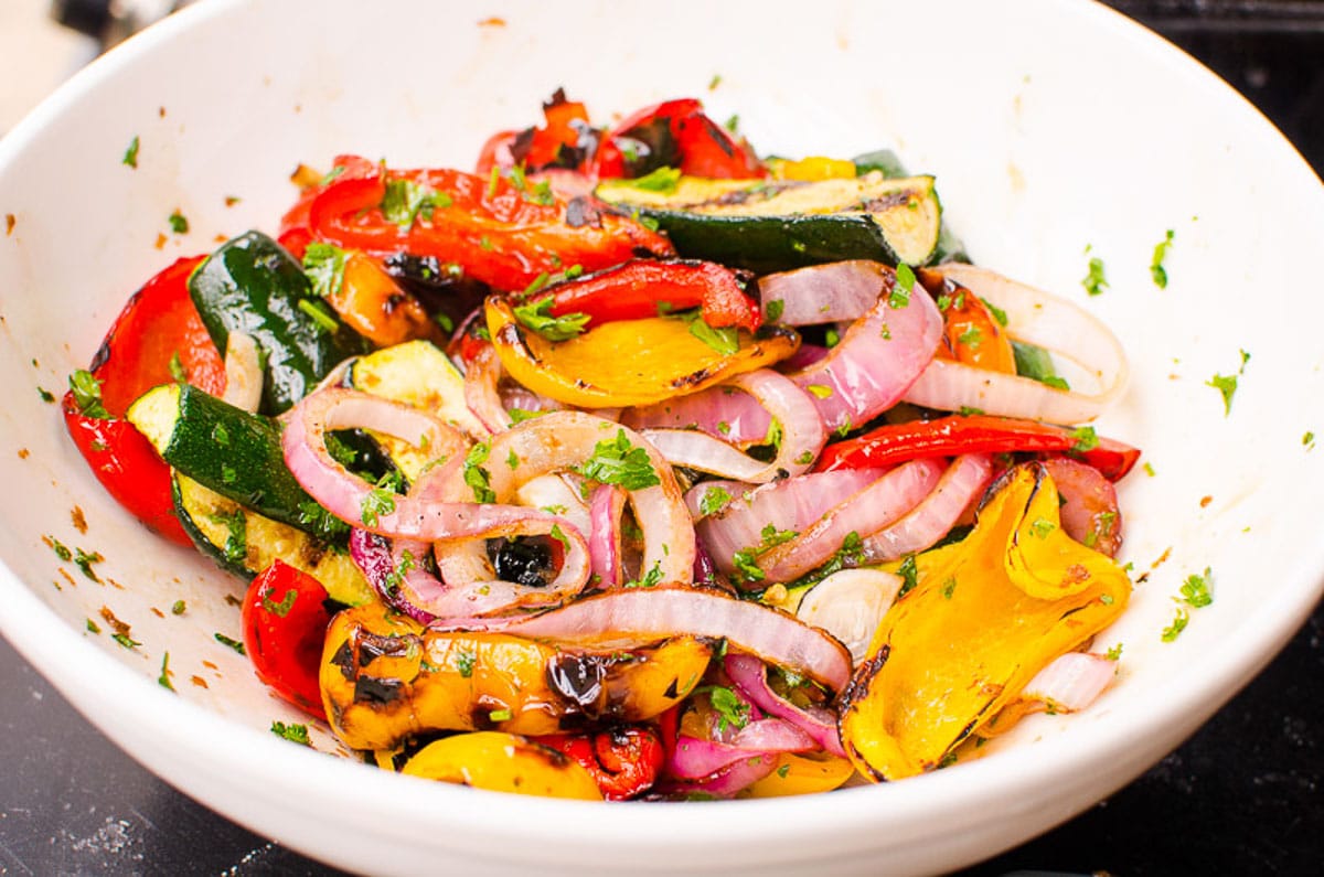Balsamic marinade tossed with grilled vegetables and parsley in white bowl.