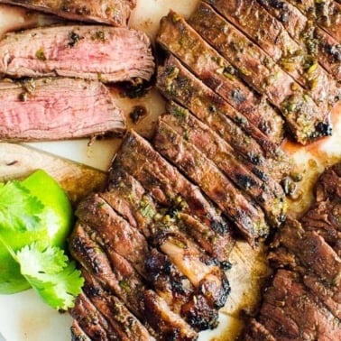Sliced carne asada steak with cilantro and lime.