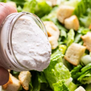 Pouring healthy caesar dressing over a bowl with Romaine lettuce, croutons and parmesan cheese.