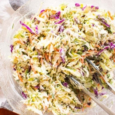 Healthy coleslaw in glass bowl with tongs.