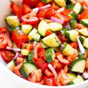 Cucumber and tomato salad with red onion and dill in white bowl.