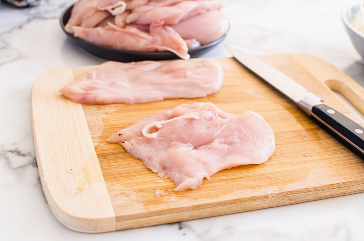 Chicken breasts cut in half on cutting board with knife.